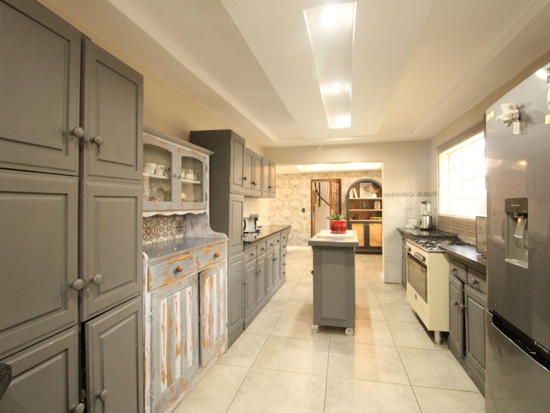A spacious kitchen featuring grey built-in cabinetry, a central island, gas stove, and tiled flooring with recessed ceiling lighting.