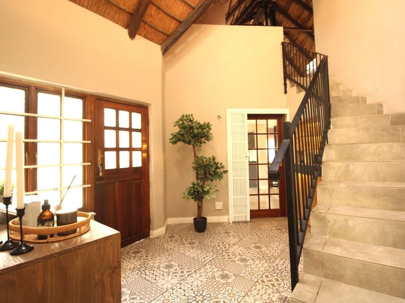 Welcoming entrance hall featuring a high thatched ceiling with exposed rafters, patterned floor tiles, and a staircase with a wrought iron balustrade.