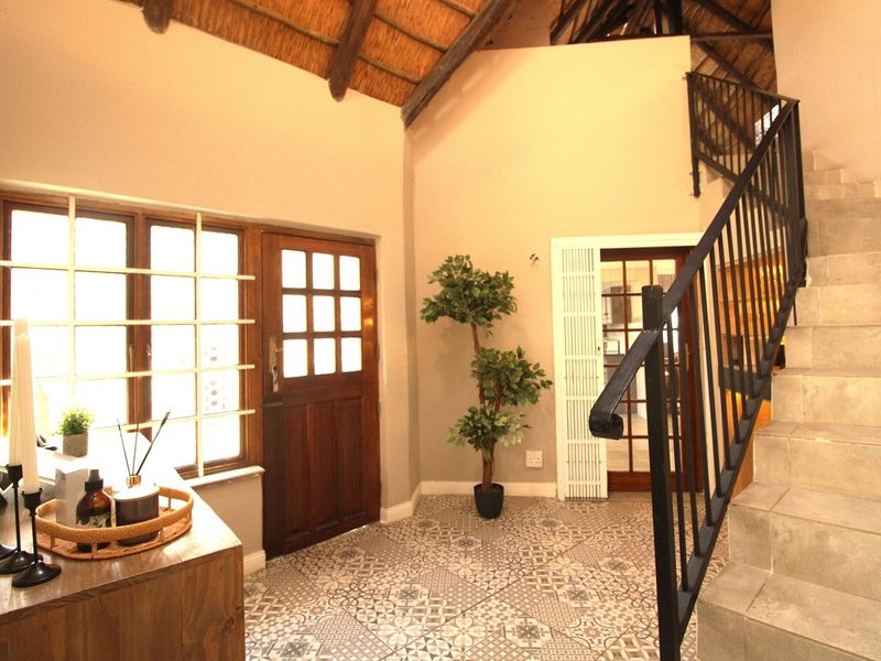 Welcoming entrance hall featuring a double-volume ceiling with exposed timber rafters, decorative tiled flooring, and a staircase with a modern metal balustrade.