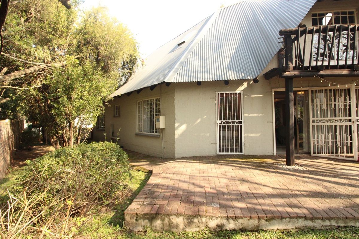 Rear view of the property featuring a corrugated metal roof, a brick paved patio area, and a timber balcony structure.