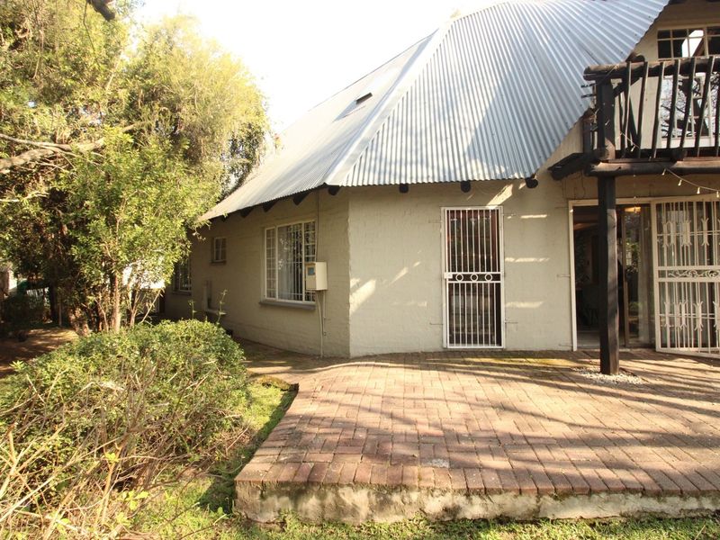 Rear view of the property featuring a corrugated metal roof, a brick paved patio area, and a timber balcony structure.