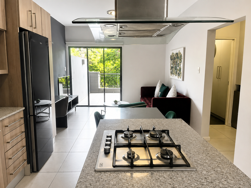 Modern open-plan kitchen and living area featuring a central island with gas hob, sleek cabinetry, and direct access to a private balcony.