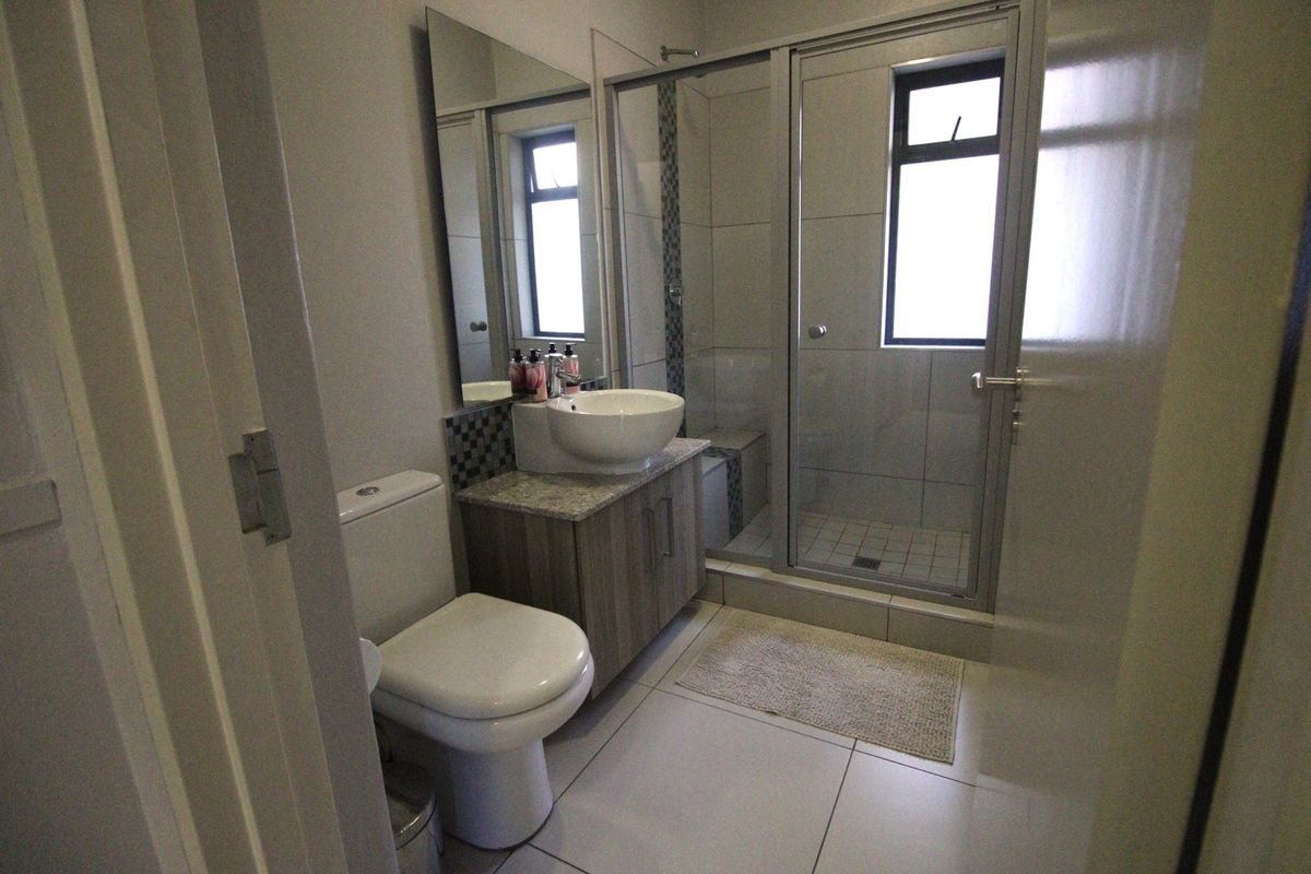 A modern bathroom featuring a vessel sink on a granite-topped vanity, a glass-enclosed shower, and neutral floor tiles.