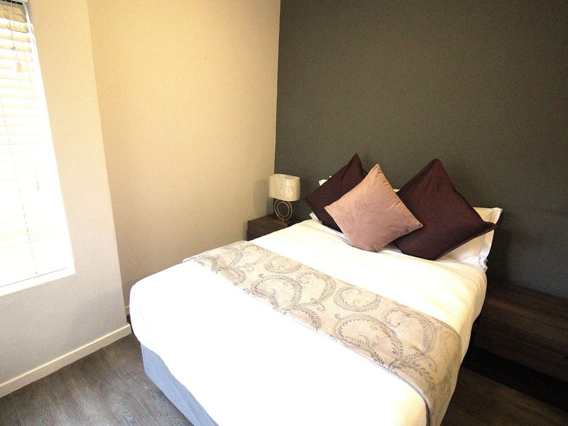 A well-maintained bedroom featuring modern laminate flooring, a dark grey accent wall, and venetian blinds for natural light control.