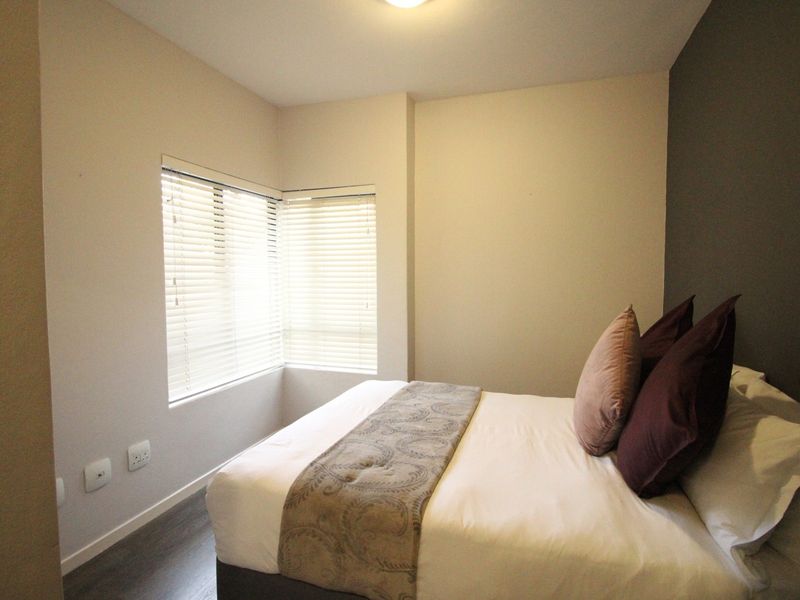 A well-maintained bedroom featuring laminate flooring, an accent wall, and corner windows fitted with venetian blinds.