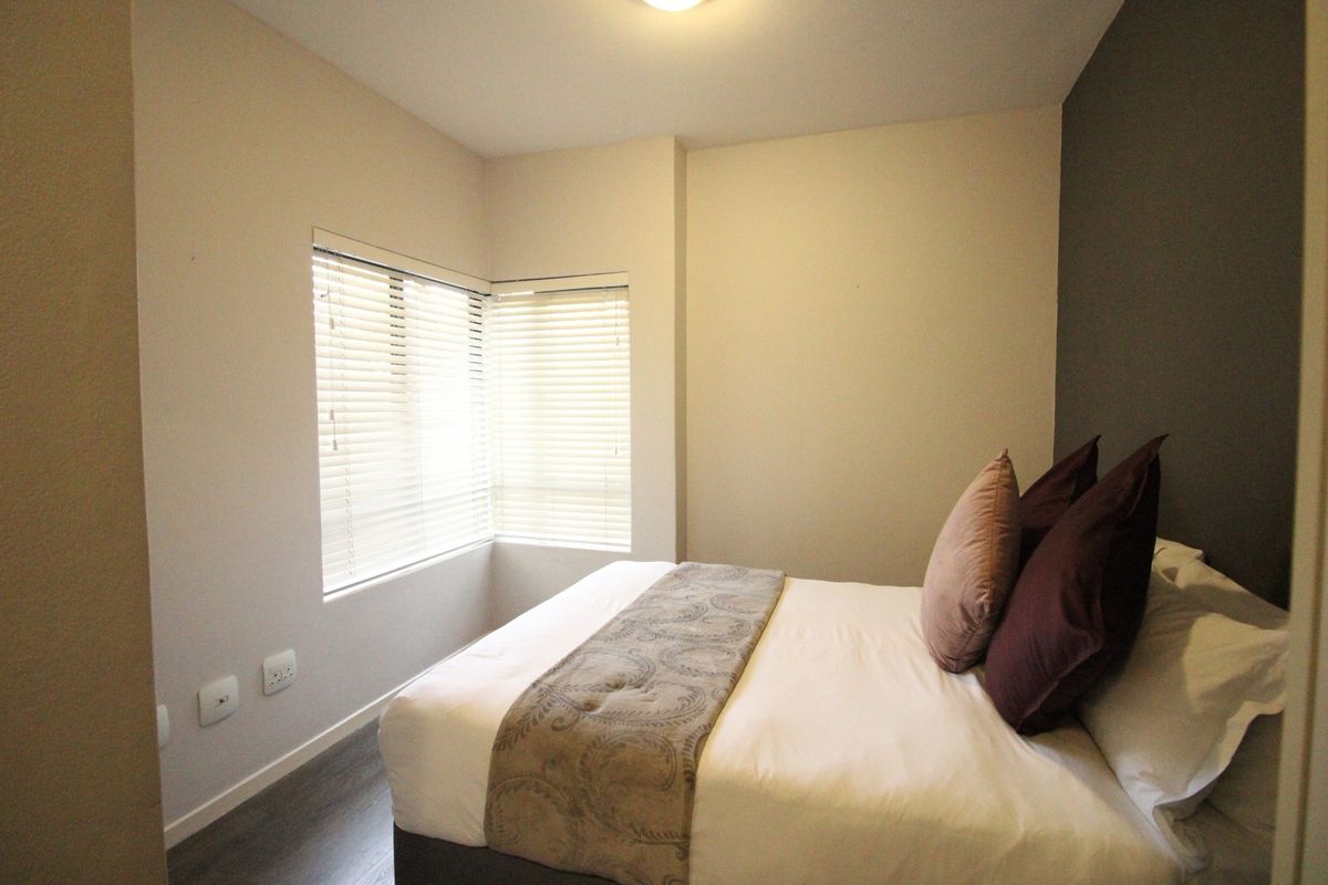 A well-maintained bedroom featuring laminate flooring, an accent wall, and corner windows fitted with venetian blinds.