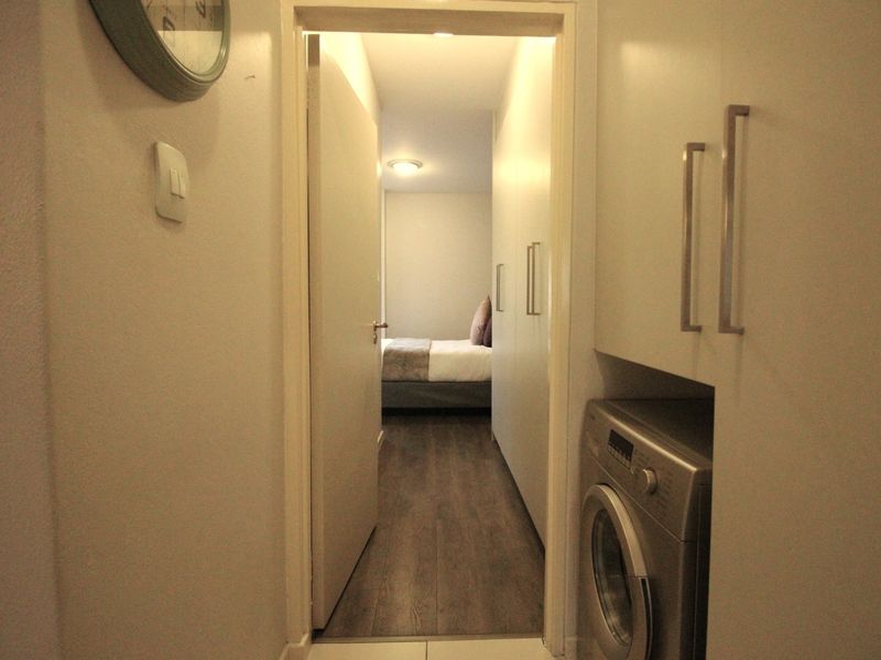 A compact laundry area featuring built-in cabinetry and integrated appliance space, providing a functional transition between the hallway and the bedroom.