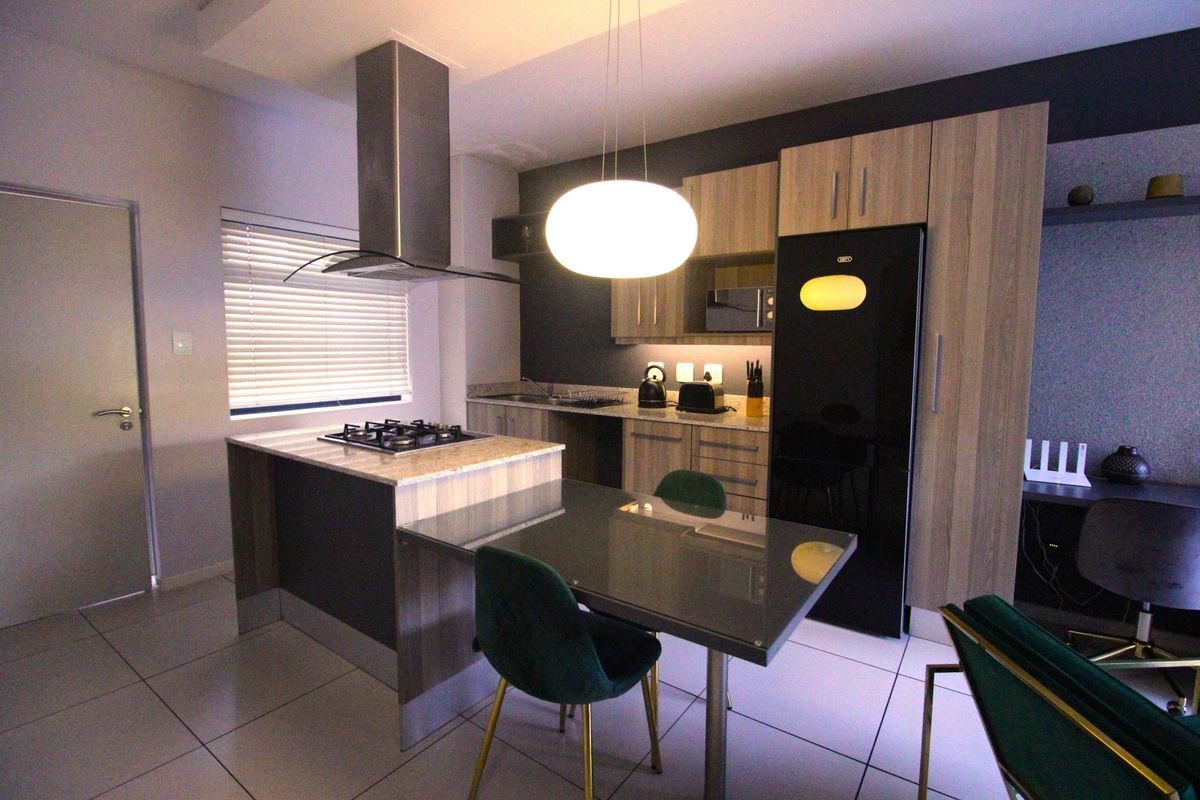 Modern kitchen featuring wood-finish cabinetry, stone countertops, a gas hob with stainless steel extractor, and integrated appliances in an open-plan layout.
