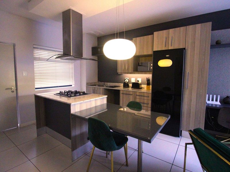 Modern kitchen featuring wood-finish cabinetry, stone countertops, a gas hob with stainless steel extractor, and integrated appliances in an open-plan layout.