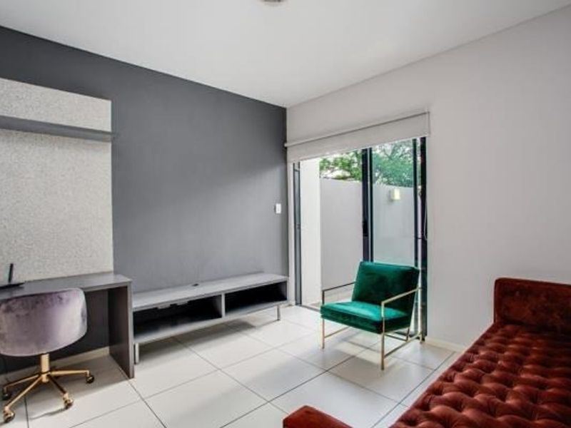 A modern living area featuring tiled floors, a built-in desk, a media console, and a sliding glass door leading to an outdoor space.