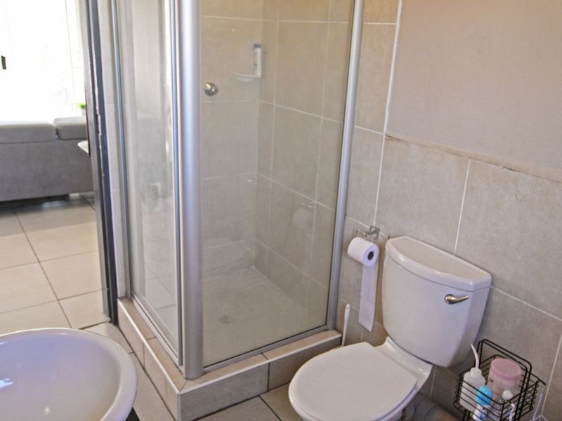A functional bathroom featuring a glass shower enclosure, a standard toilet, and tiled finishes throughout.