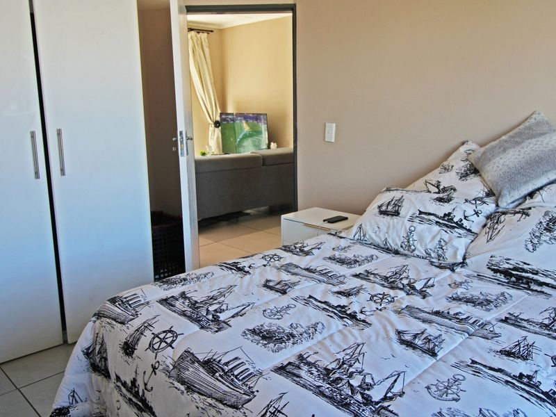 A bedroom featuring built-in wardrobes and tiled flooring, with a view through the doorway into the adjacent living area.
