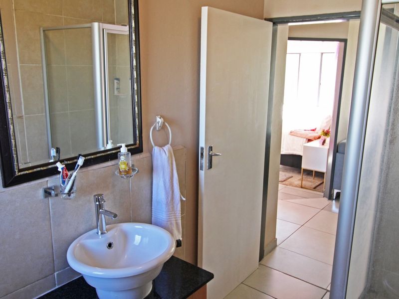 A functional bathroom featuring a basin with vanity, tiled walls and flooring, and a shower enclosure, with a view into the adjacent bedroom.