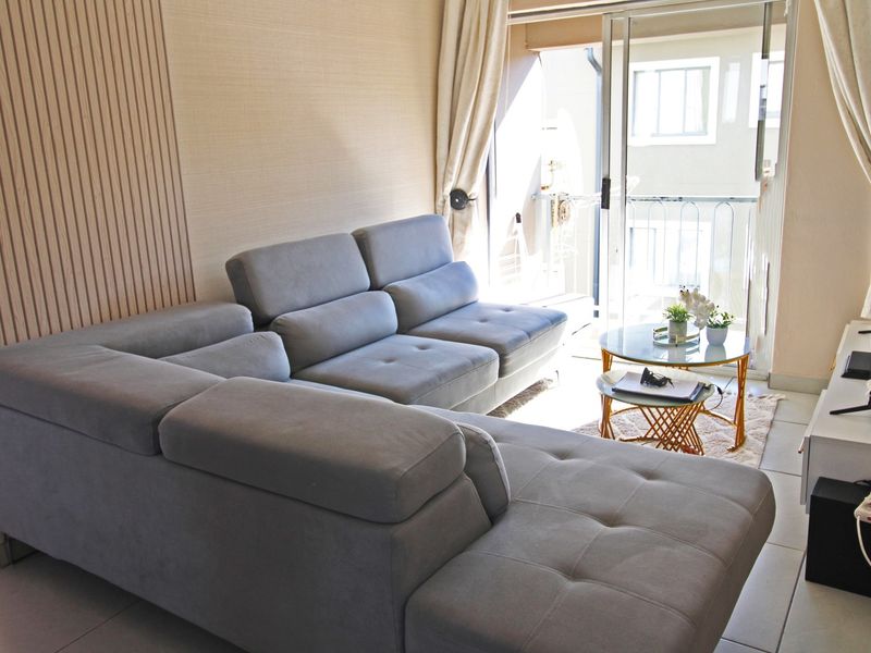 A well-lit living room featuring modern slatted wood wall paneling, tiled flooring, and a sliding glass door providing access to a balcony.