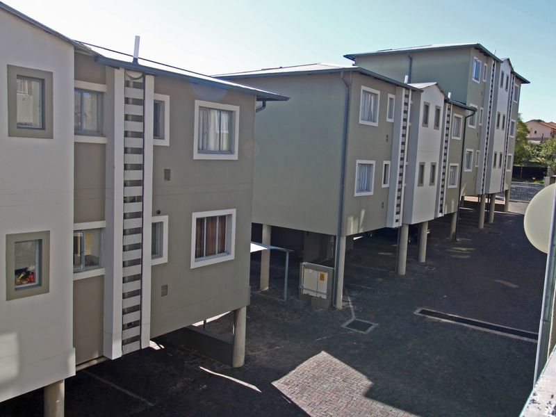 Exterior view of a multi-story apartment complex featuring stilted building design and paved ground-level parking areas.