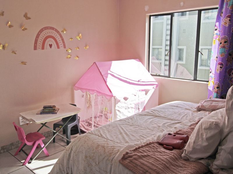 A bedroom featuring tiled flooring and an aluminium-framed window, currently decorated as a child's room with visible wall surface imperfections.