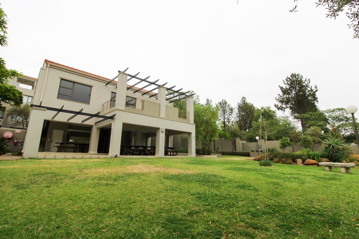 Rear view of the apartment building featuring a covered patio, upper balcony with pergola, and a well-maintained garden area.