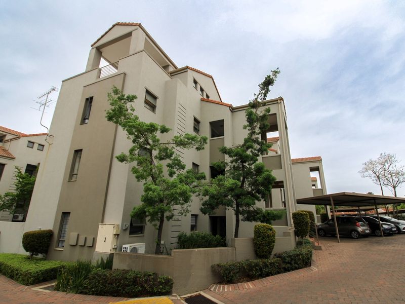 Exterior view of a multi-story apartment complex featuring terracotta roof tiles, paved driveway, and covered parking facilities.