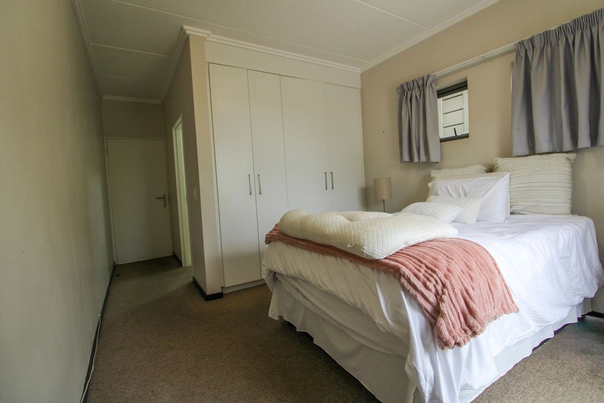 A functional bedroom featuring built-in cupboards, carpeted flooring, and a louver window, providing a comfortable and practical living space.