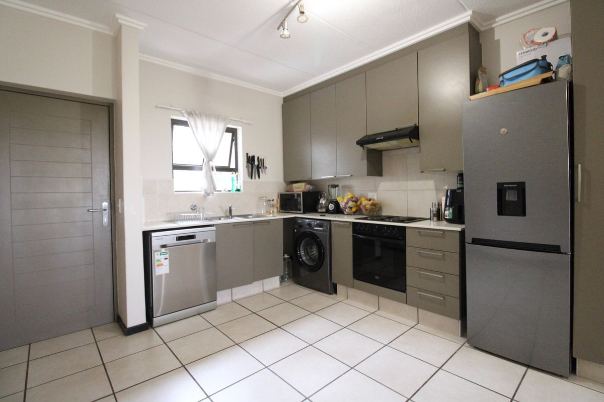 A functional kitchen featuring modern grey cabinetry, built-in oven and hob, extractor fan, and tiled flooring with integrated appliance spaces.