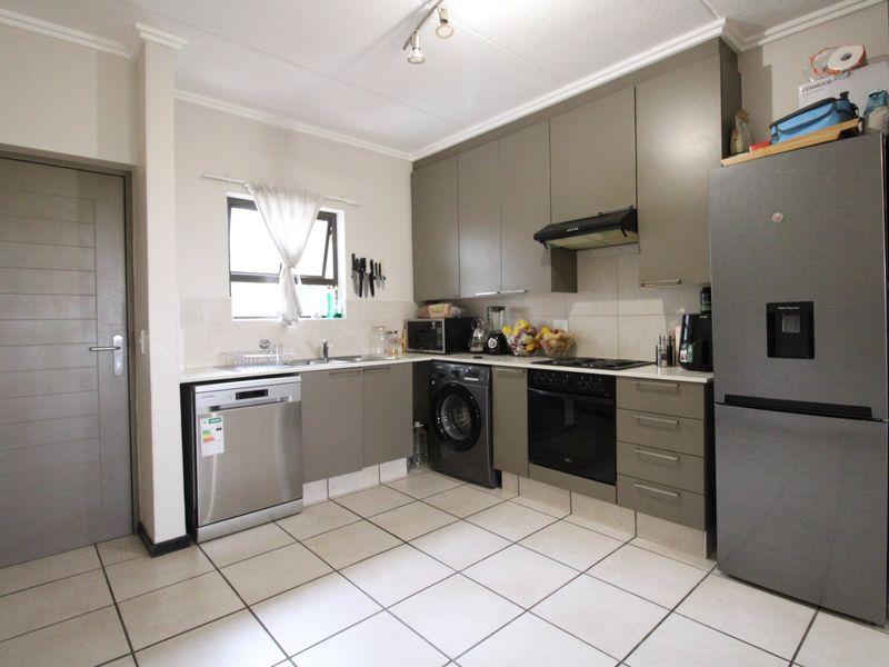 A functional kitchen featuring modern grey cabinetry, built-in oven and hob, extractor fan, and tiled flooring with integrated appliance spaces.
