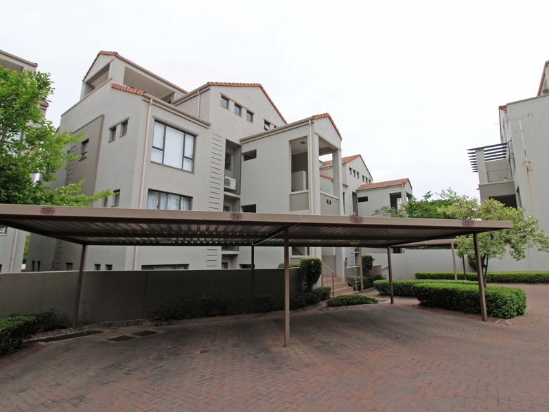 Exterior view of the apartment complex featuring a covered carport, paved driveway, and well-maintained landscaped garden areas.
