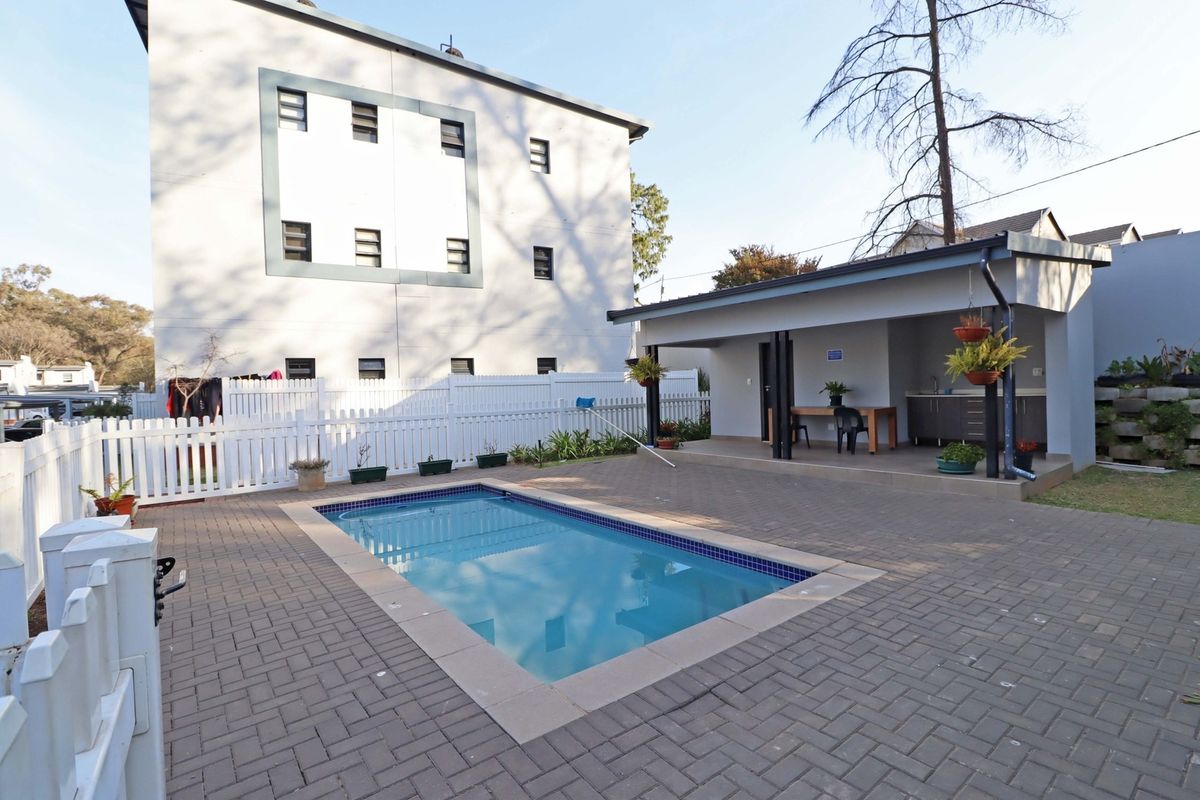 Outdoor pool area featuring a paved patio, a covered entertainment space with a sink, and a white picket fence enclosure.