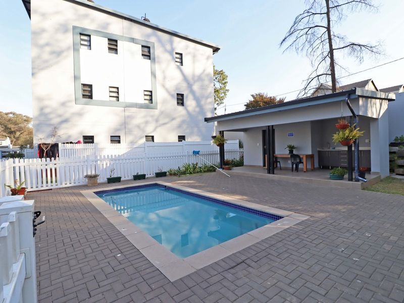 Outdoor pool area featuring a paved patio, a covered entertainment space with a sink, and a white picket fence enclosure.