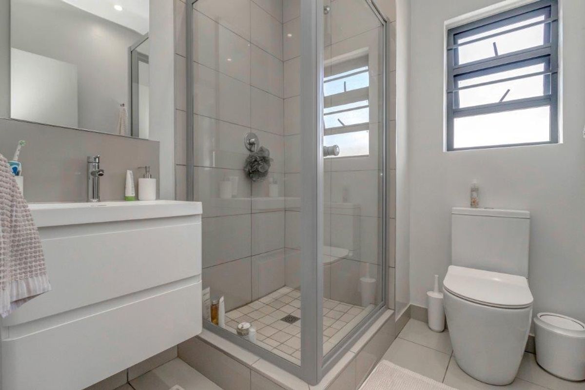 Modern bathroom featuring a sleek vanity, a glass-enclosed shower, and a contemporary toilet with neutral wall and floor tiling.