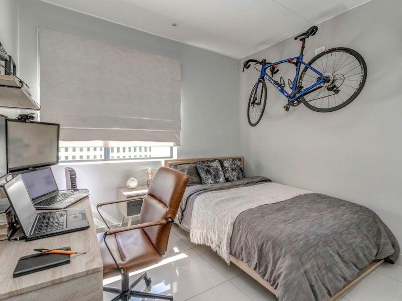 A well-maintained bedroom featuring tiled flooring, neutral wall finishes, and built-in shelving, currently utilized as a combined sleeping and workspace area.