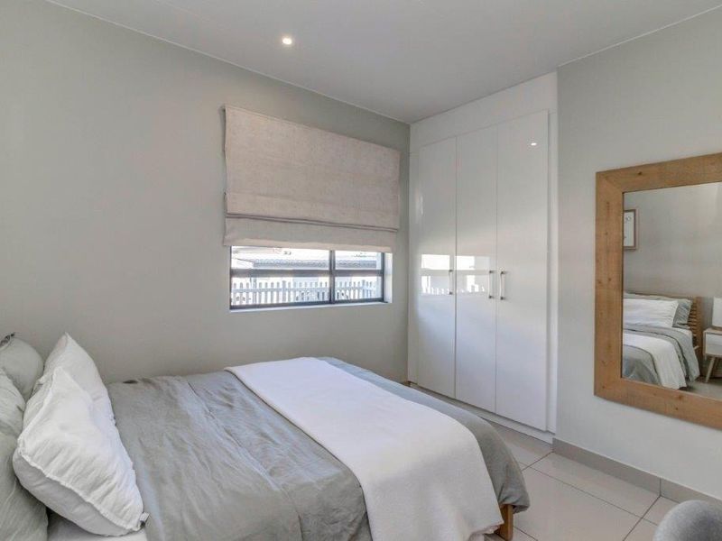 A modern, well-maintained bedroom featuring neutral tones, sleek built-in cupboards, tiled flooring, and recessed lighting.