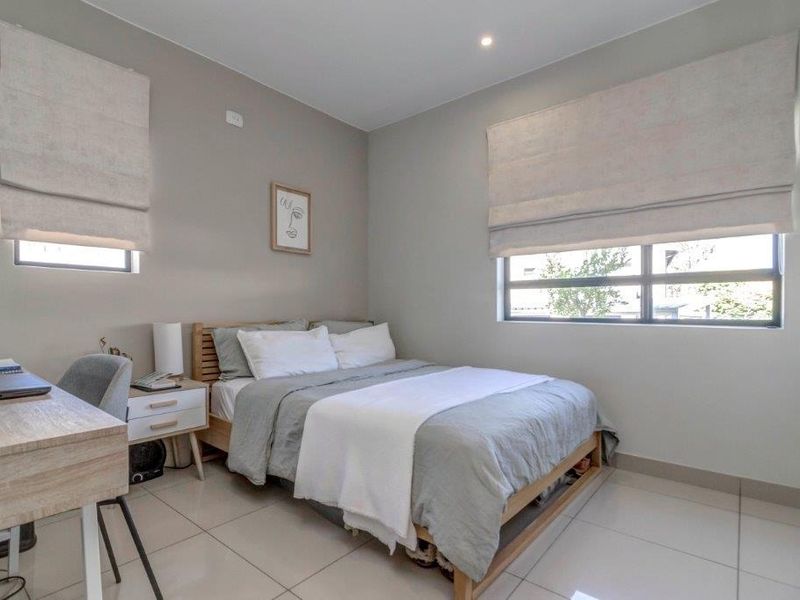A well-maintained bedroom featuring neutral wall tones, large format floor tiles, recessed lighting, and fitted roman blinds.