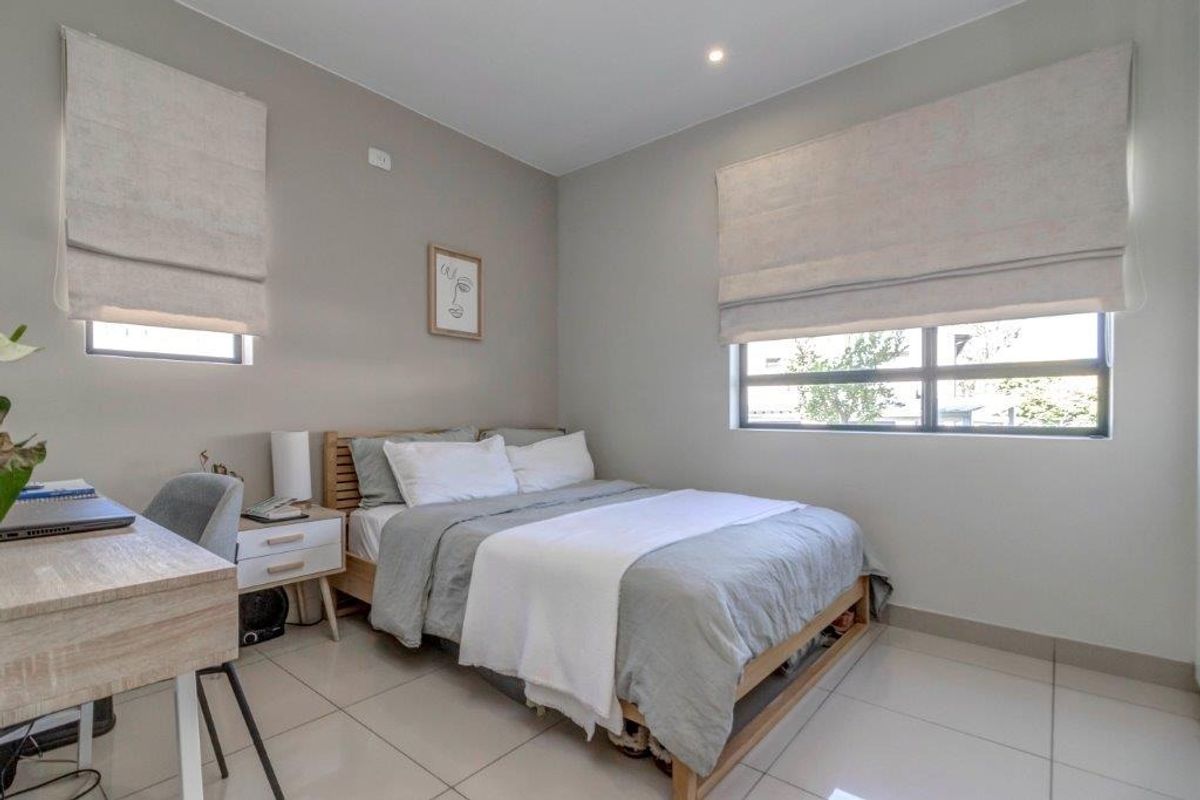 A well-maintained bedroom featuring neutral wall tones, large format floor tiles, recessed lighting, and fitted roman blinds.