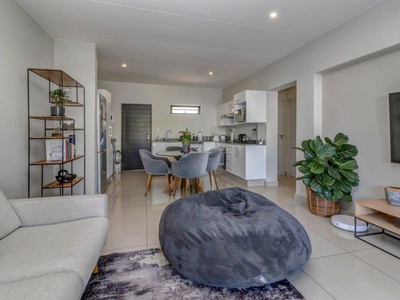 A modern open-plan living and kitchen area featuring neutral tiled flooring, recessed lighting, and clean white cabinetry in a well-maintained apartment setting.