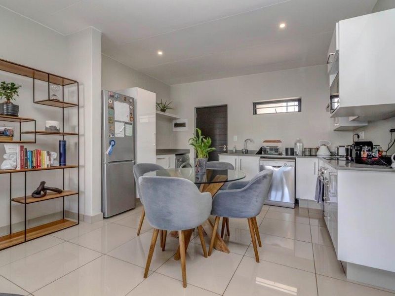 Modern open-plan kitchen and dining area featuring sleek white cabinetry, stone countertops, tiled flooring, and recessed lighting in a contemporary apartment setting.