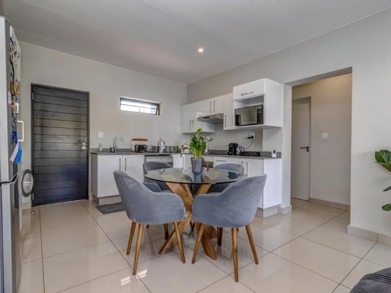 Modern open-plan kitchen featuring white cabinetry, integrated appliances, and sleek tiled flooring, seamlessly flowing into the dining area.