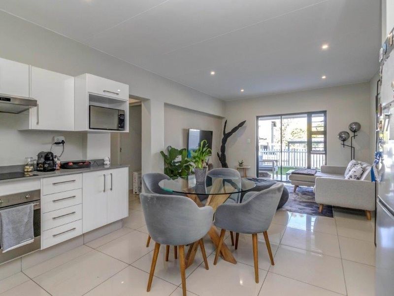 Modern open-plan living area featuring a sleek kitchen with built-in appliances, tiled flooring, and seamless access to a private balcony through sliding glass doors.