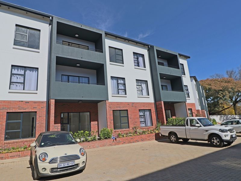 Front elevation of a modern multi-story apartment complex featuring brick and rendered facade, private balconies, and a paved parking area.
