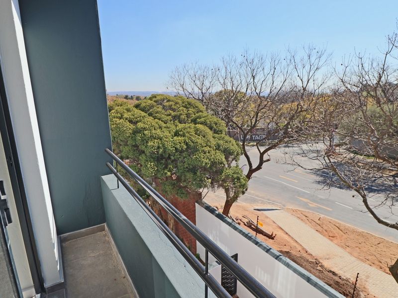 A clean, modern apartment balcony featuring a metal balustrade and tiled flooring, offering an elevated view of the surrounding street and landscape.