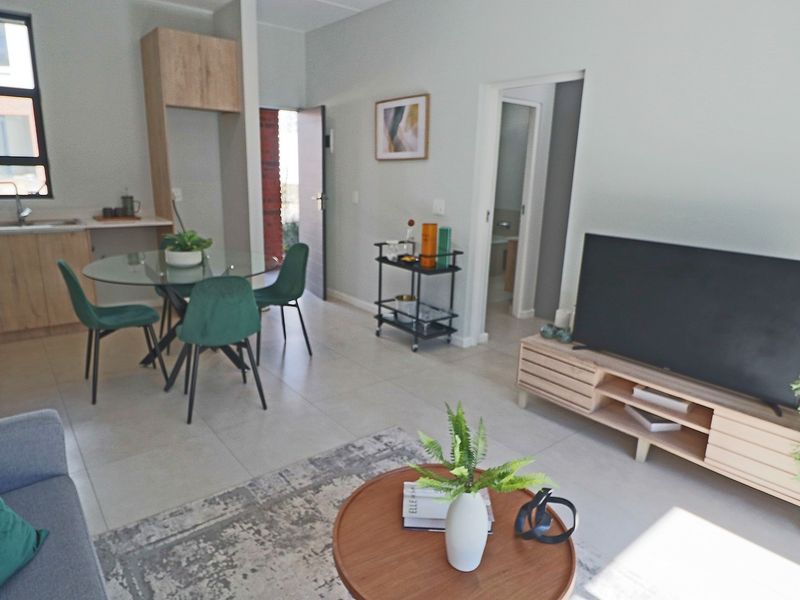 An open-plan living and kitchen area featuring modern light wood cabinetry, neutral tiled flooring, and direct access to adjacent rooms.