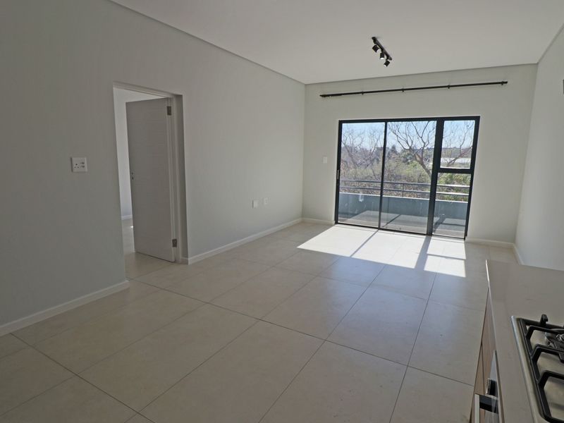 Bright open-plan living area featuring large format floor tiles, modern track lighting, and a sliding glass door leading to a private balcony.