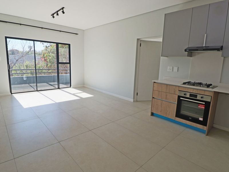 Modern open-plan living area featuring a sleek kitchen with built-in appliances, tiled floors, and a large sliding door leading to a balcony.