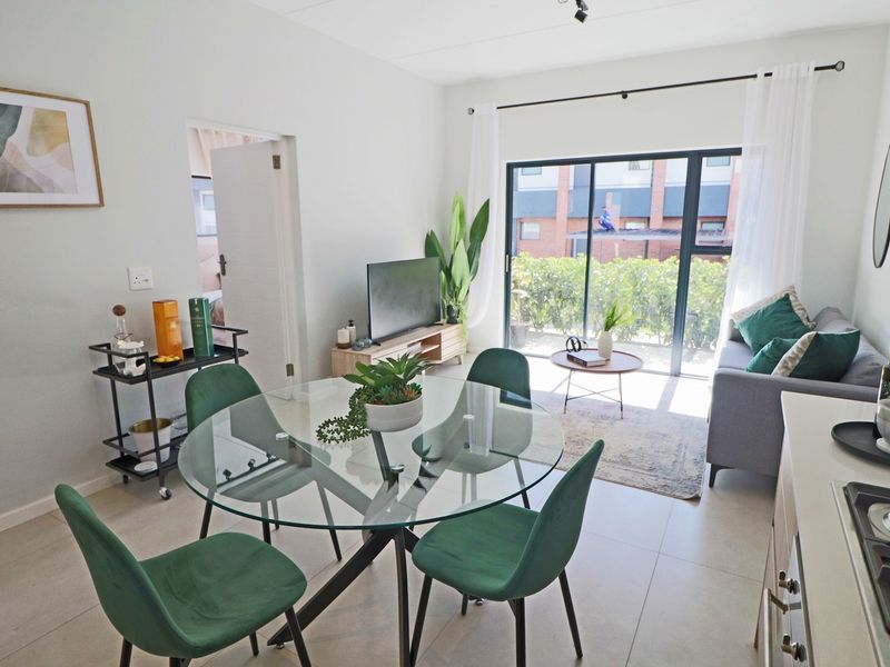 Bright open-plan living and dining area featuring tiled floors, modern kitchen finishes, and large sliding glass doors leading to an outdoor space.