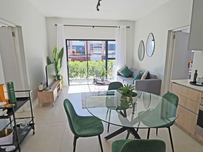 Modern open-plan living and dining area featuring sleek kitchen cabinetry, built-in oven, and large sliding glass doors leading to an outdoor space.