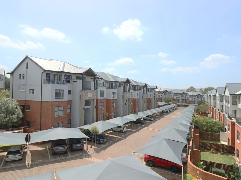 An elevated view of a modern apartment complex featuring brick and plaster facades, metal roofing, and extensive covered parking bays.