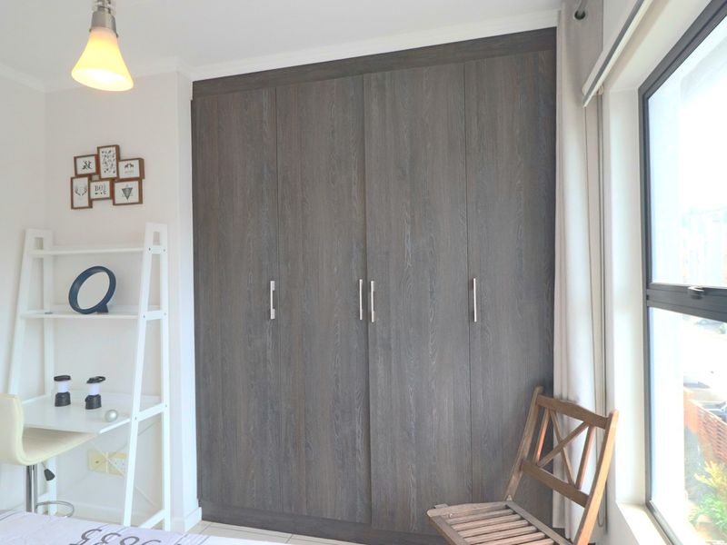 A bedroom featuring dark wood-finish built-in cupboards and a large window providing natural light.