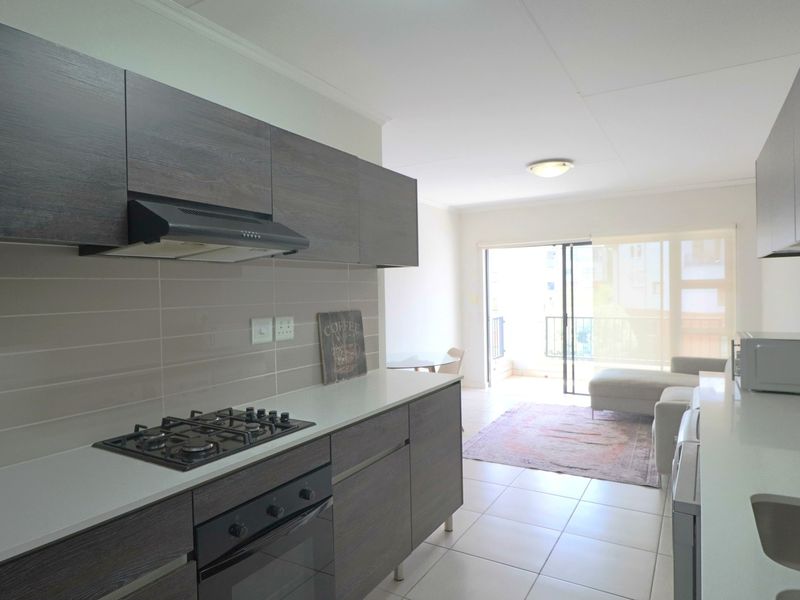 Modern open-plan kitchen featuring dark wood cabinetry, gas hob, and built-in oven, flowing into a bright living area with balcony access.