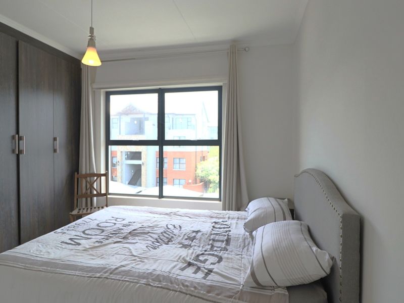 A well-lit bedroom featuring a large built-in wardrobe, neutral wall finishes, and a window with views of the surrounding apartment complex.