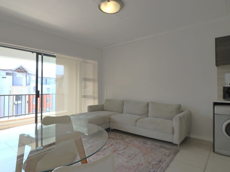 Open-plan living area featuring tiled floors, a sliding door leading to a balcony, and a dedicated space for laundry appliances.