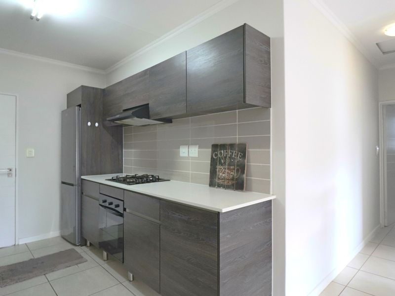 Modern kitchen featuring dark wood-grain cabinetry, stone countertops, a gas hob, built-in oven, and a neutral tiled backsplash.